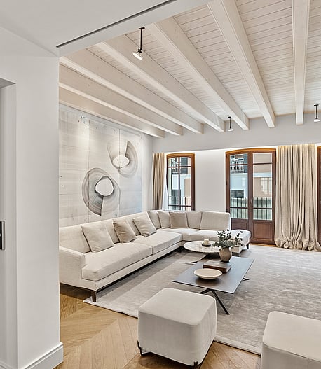 Bright living room with herringbone wood flooring, white sectional sofa, and tall wooden French doors under a beamed ceiling.