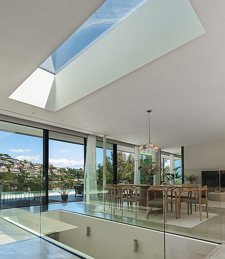 Modern living and dining room featuring floor-to-ceiling glass walls, a large skylight, and views of Son Vida hills.
