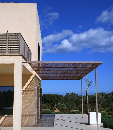 Exterior terrace of a Mallorcan finca with a metal laser-cut pergola casting intricate shadows on the stone floor.