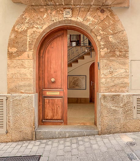 An arched timber front door set within a traditional natural stone facade on a cobblestone Old Town street.