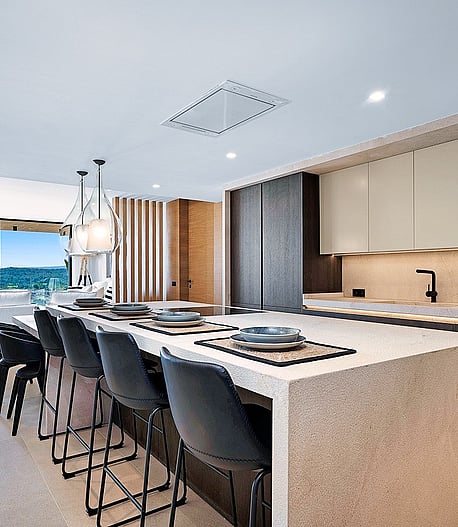 Modern kitchen with large white stone island, dark bar stools, and sliding glass doors opening to a mountain terrace.