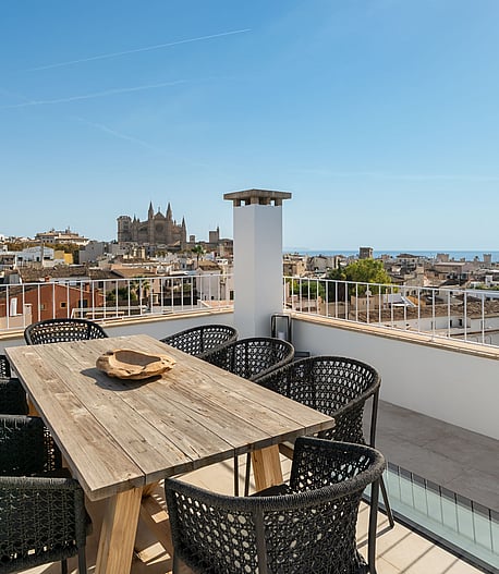 Rooftop terrace with wooden dining table and black chairs overlooking Palma Cathedral and the Mediterranean sea.