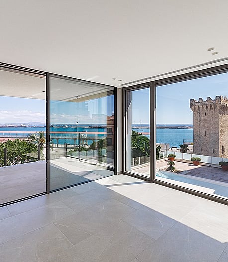 Light-filled corner living space with floor-to-ceiling glass on two elevations framing Palma harbour and open sea