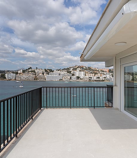 A spacious grey-tiled terrace with black metal railings faces a bay filled with boats under a cloudy sky.