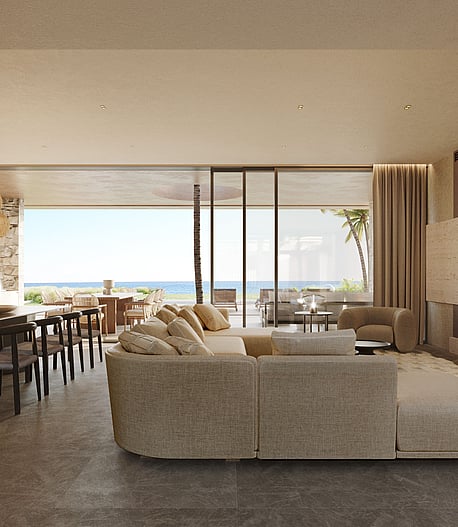 Wide-angle shot of a bright, open-plan living and dining room with floor-to-ceiling glass walls leading to an outdoor terrace, limestone fireplace, and Mediterranean sea views.