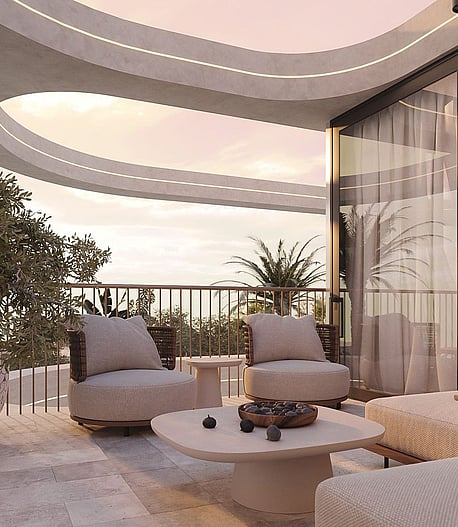 A modern curved terrace overlooking the sea at sunset, featuring stone flooring, outdoor seating, and a large potted plant.