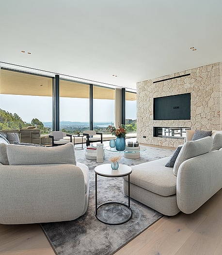 Contemporary living room with light oak floors, a textured stone fireplace wall, and floor-to-ceiling windows facing the sea.