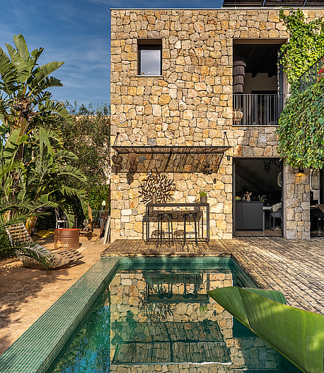 Exterior view of a stone-clad villa in Genova featuring a rectangular swimming pool, lush greenery, and climbing vines.