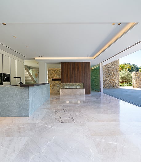 Modern open-plan kitchen with a stone island, floor-to-ceiling sliding glass doors, and polished marble flooring.