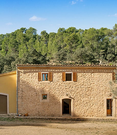 Two-storey stone finca façade with wooden shutters and dry-stone walls