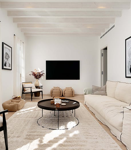 Living room with black cane armchairs, a cream linen sofa, black round coffee tables and framed black and white photography.