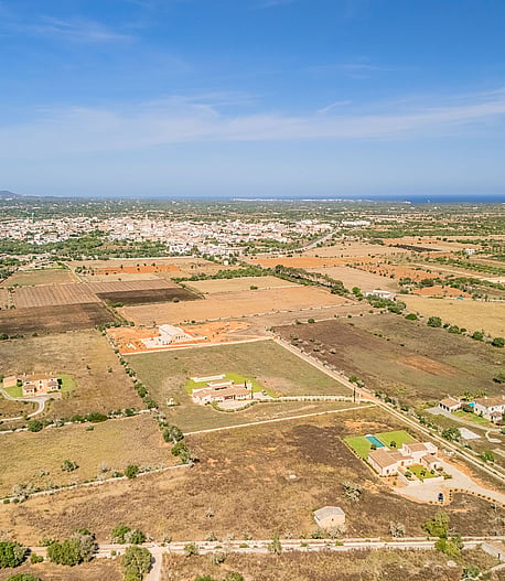 High-altitude aerial view of rural Mallorcan landscape near Santanyí, featuring sparse vegetation and distant town buildings.