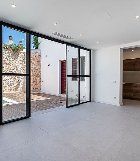 Modern open-plan living room with large floor-to-ceiling sliding glass doors opening onto a stone-walled terrace with a plunge pool.