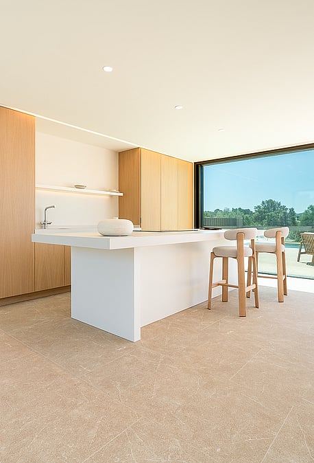 Modern open-plan kitchen with white island, light wood cabinetry, and floor-to-ceiling sliding glass doors opening to a terrace.