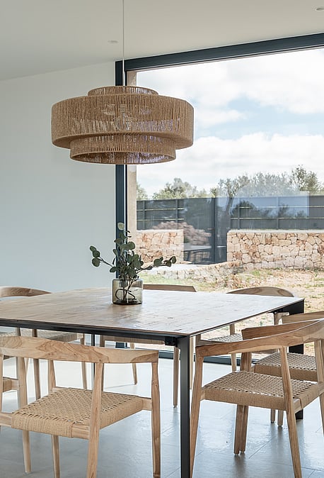 Dining area featuring a wooden table, woven chairs, and a large pendant light set against a window with mountain scenery.