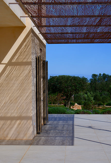 A modern outdoor terrace in Santanyí featuring a geometric laser-cut metal pergola casting intricate shadows on stone walls.