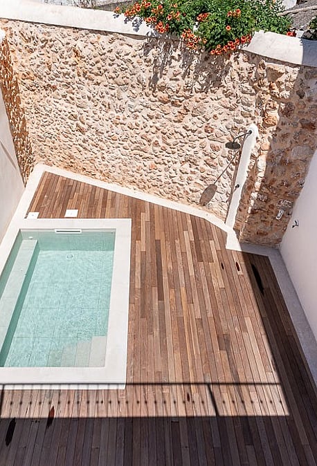 High-angle view of a small rectangular plunge pool surrounded by a wooden deck and high white walls with a natural stone feature wall.