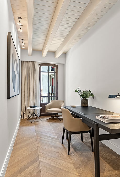 Minimalist home office featuring chevron wood flooring, exposed timber beams, a dark desk, and an arched glass door.