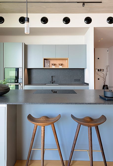 Contemporary kitchen featuring a grey island, dark stone countertops, wooden bar stools, and track lighting in a penthouse.