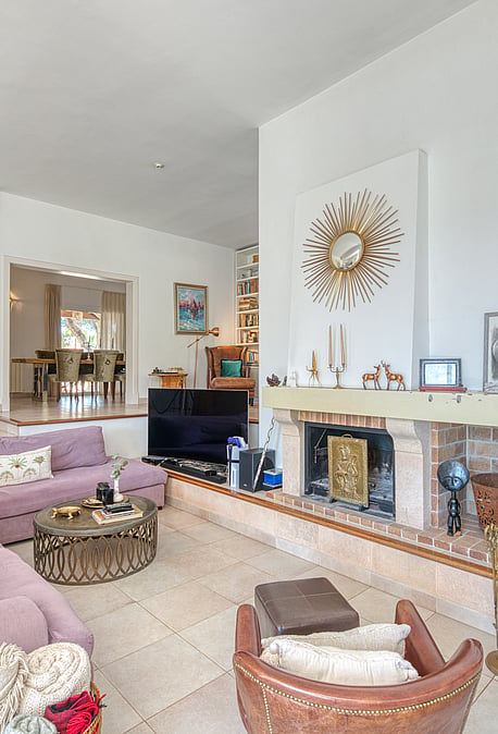 Spacious living room featuring a large lilac sectional sofa, a stone-fronted fireplace, and a light-colored tiled floor.