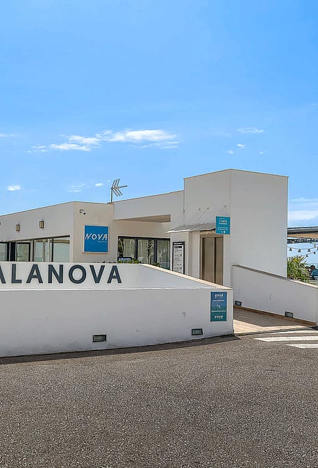 Exterior view of the white facade and entrance signage for Port Calanova under a clear blue sky.