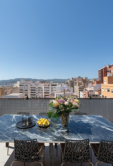 Outdoor dining table with marble top on a rooftop terrace overlooking Old Town buildings under a clear blue sky.