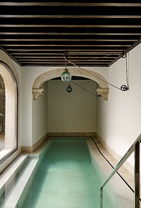 Indoor swimming pool featuring turquoise water, arched stone vault ceiling detail, minimalist contemporary design, and soft natural light