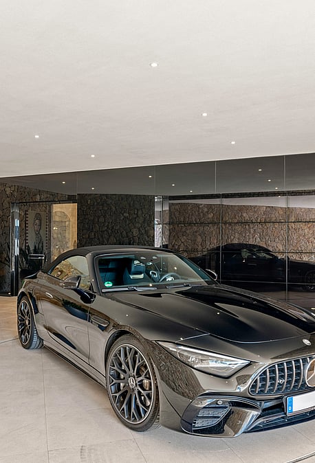 A luxury garage interior featuring a dark sports car on a mechanical turntable, flanked by natural stone walls and planters.