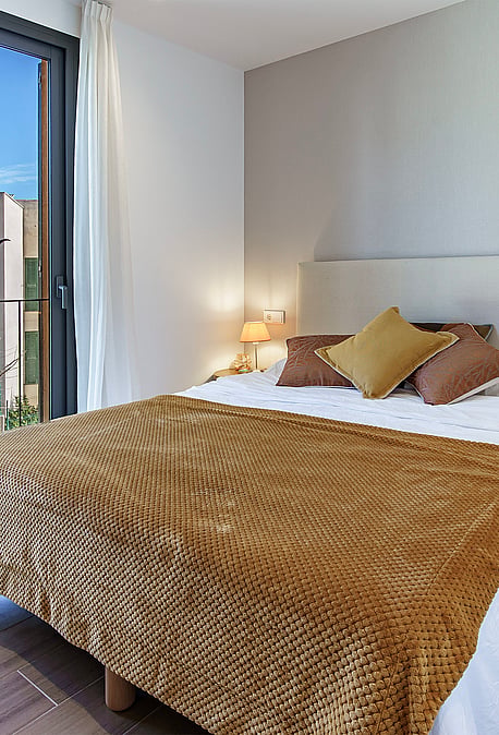 A contemporary bedroom with a double bed, brown patterned throw, and a sliding glass door opening to a small balcony.