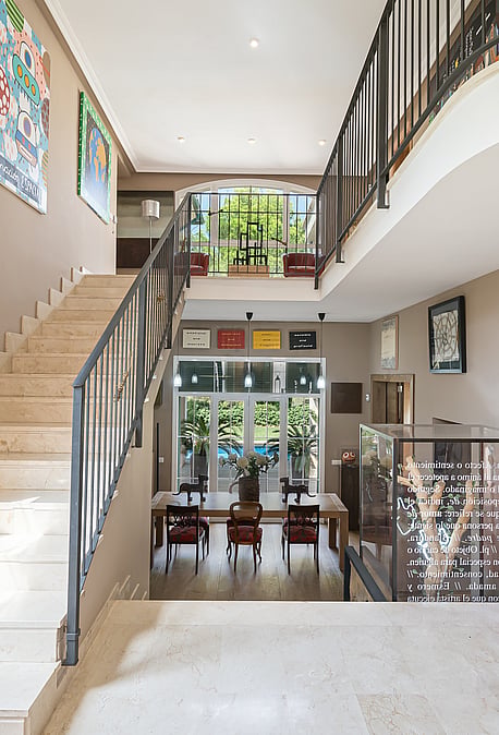 An expansive entrance hall with a polished stone staircase and ornate metal railings, looking towards a dining area beyond.