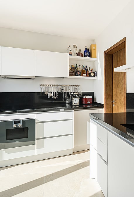 Bright modern kitchen with white handleless cabinets, black granite worktops, and stainless steel Gaggenau appliances.