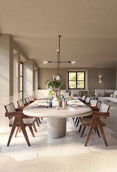 Dining room with a large oval stone table and wooden chairs, set against stone walls and large black-framed glass doors.