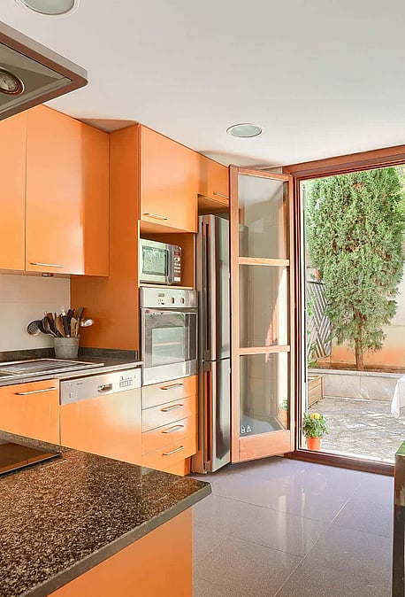 Modern kitchen with orange cabinetry, granite countertops, and glass door leading to a private outdoor garden area.