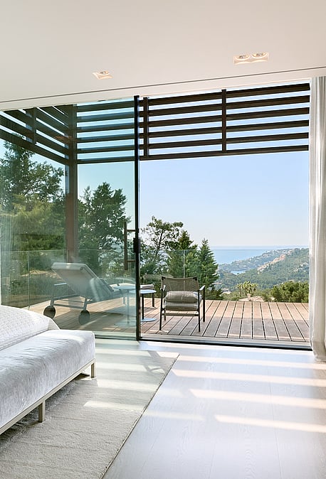 Bedroom with floor-to-ceiling glazing opening to a terrace over the sea and harbour