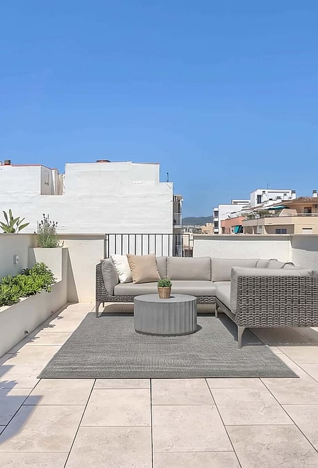A spacious rooftop terrace featuring a modular outdoor sofa set on a textured rug, bordered by a wooden screen and stone walls.