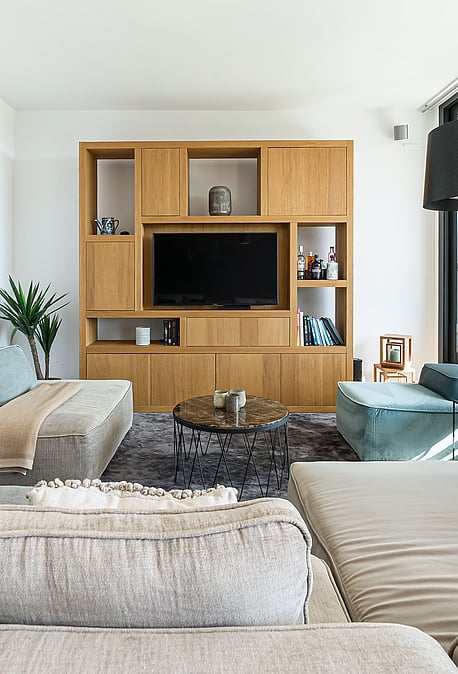 Modern living room with a large modular sofa, oak wood media wall unit, and glass sliding doors overlooking a terrace.