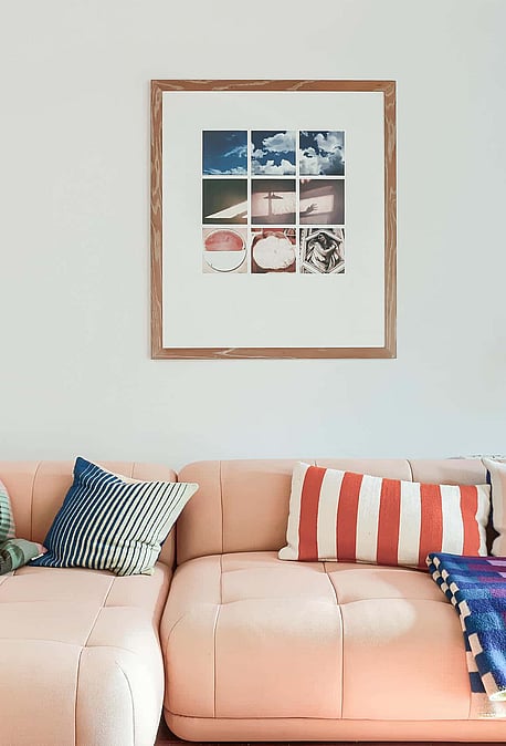 A pale pink sectional sofa sits against a plain white wall, decorated with colorful cushions and a grid-style framed print.