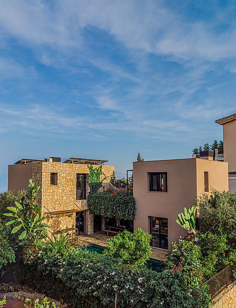 Exterior view of a multi-story villa in Genova featuring stone cladding, smooth stucco walls, and lush garden surroundings.