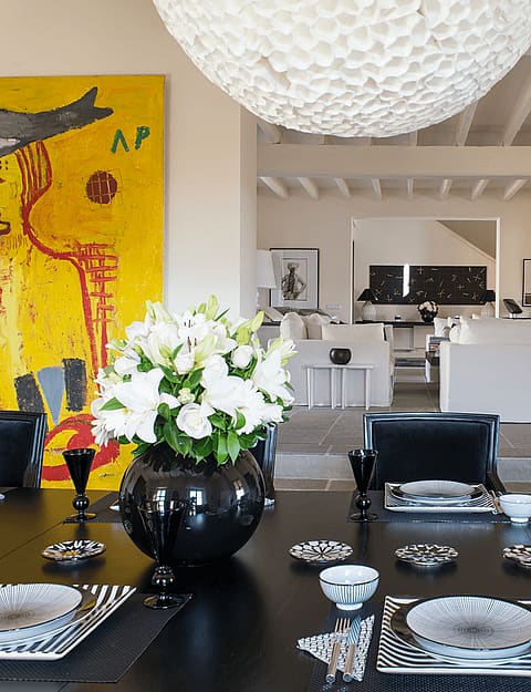 Dining room featuring a round black table, black leather chairs, and a large yellow painting on the wall.