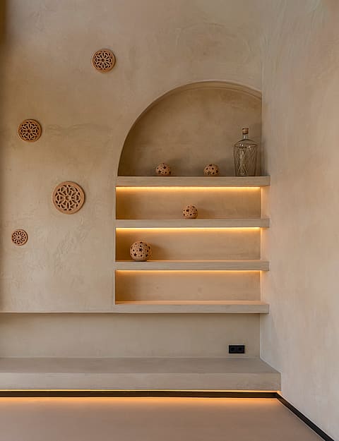 A beige textured wall featuring a recessed arched shelf system with warm LED strip lighting and decorative terracotta objects.