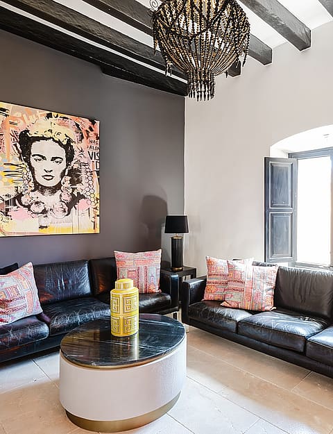 A living room with two black leather sofas facing a central coffee table, dark gray accent wall, and exposed dark ceiling beams.