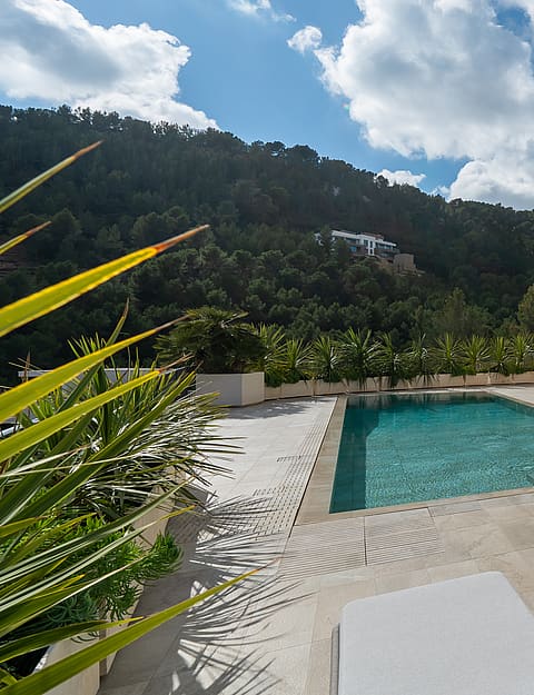 A rectangular swimming pool on a tiled terrace with white sun loungers, set against a multi-story villa with arched balconies.