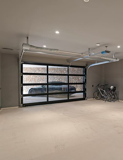 Interior view of a modern underground garage with light grey walls, concrete floors, and a metal and glass sectional door.