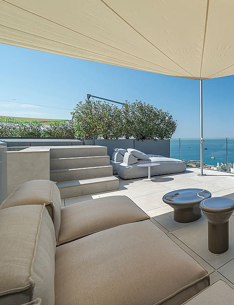 Rooftop terrace with beige modular sofas, sail shade, and panoramic sea views in Cala Mayor.