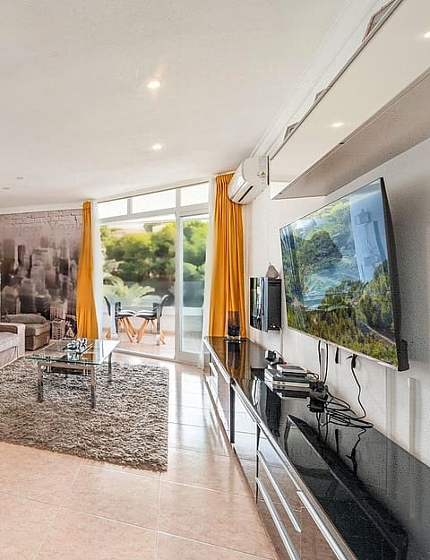 Wide-angle view of a living room featuring a plush sofa, high-gloss TV unit, and floor-to-ceiling glass doors opening to a terrace.