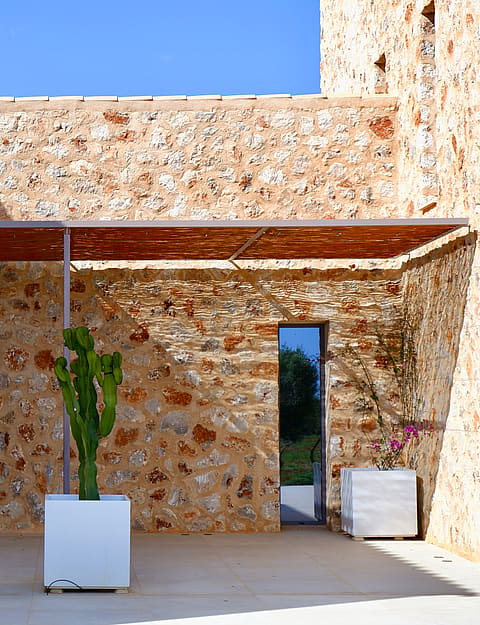 Entrance to a traditional stone-walled finca in Santanyí featuring a wooden pergola, cactus planters, and a timber door.