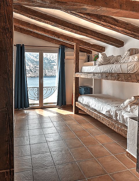 Bunk bedroom featuring exposed wood ceiling beams, tiled flooring, and brass pendant lanterns, with a view of the sea.