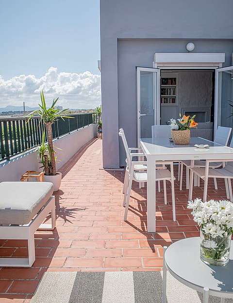 A sunlit rooftop terrace in El Molinar with a white dining set, terracotta tiles, and mountain views in the background.