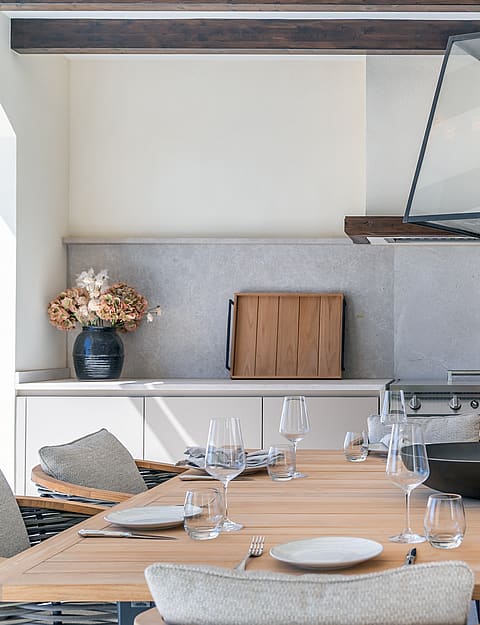 A solid oak dining table sits beneath dark wood ceiling beams and a large glass lantern pendant in a bright interior.