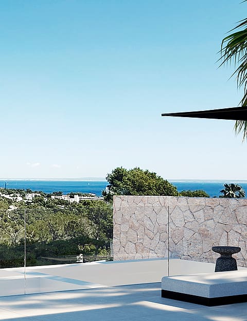 A wide terrace overlooking the Mediterranean sea with a stone retaining wall and glass railing in bright daylight.